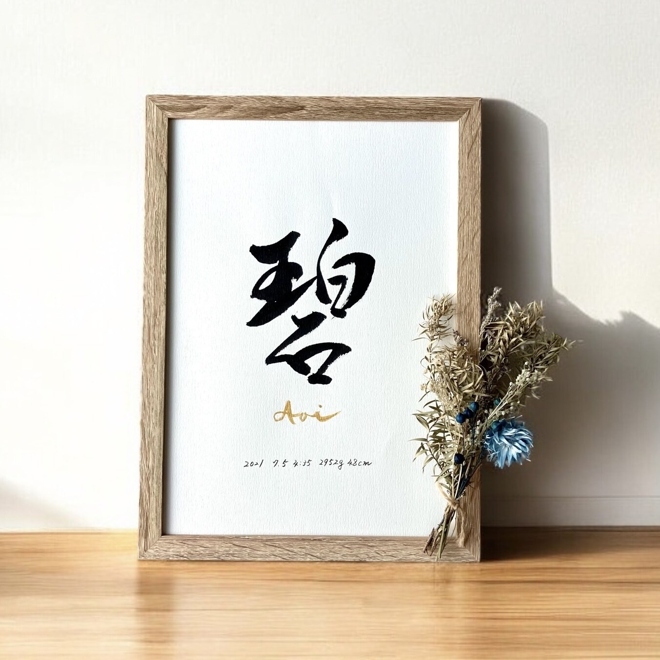 木の額縁に入った命名書。名前の筆文字とゴールドのローマ字が入っている